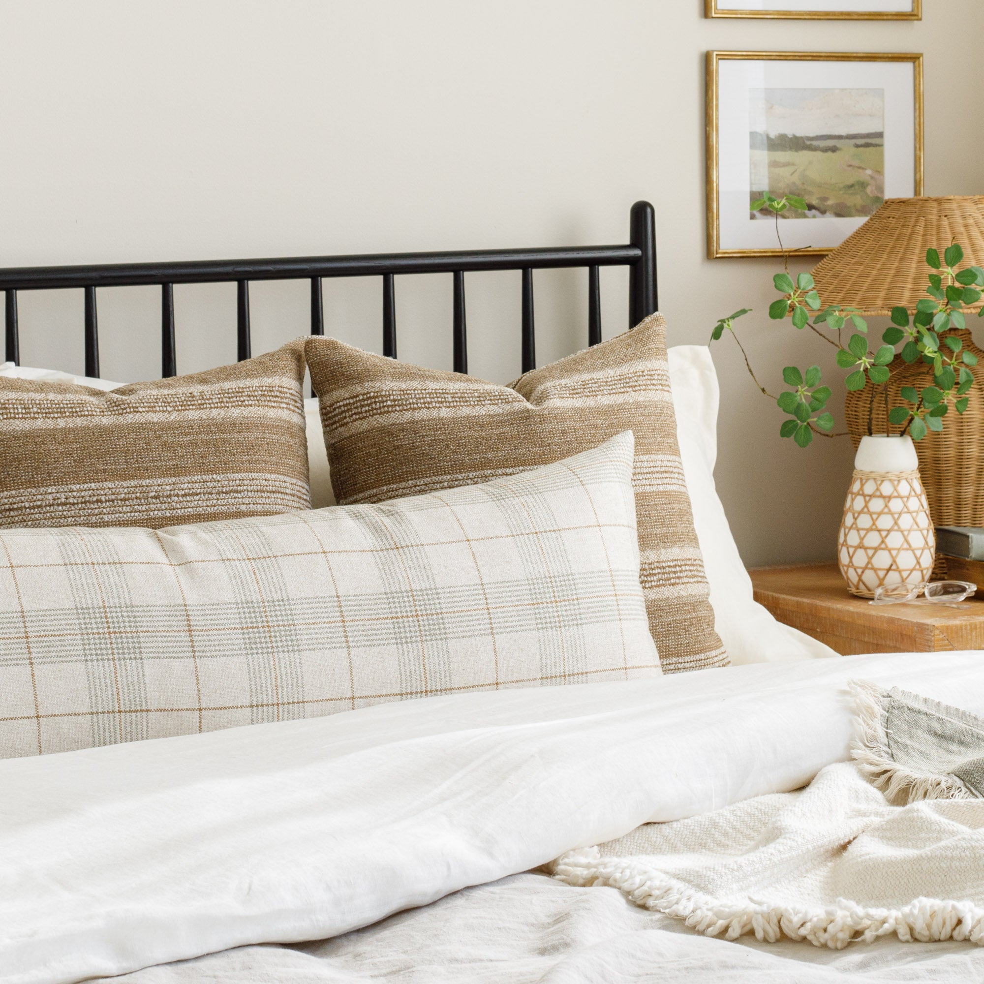 A casual plaid bolster pillow styled on a bed with 2 cozy earthy brown striped pillows.