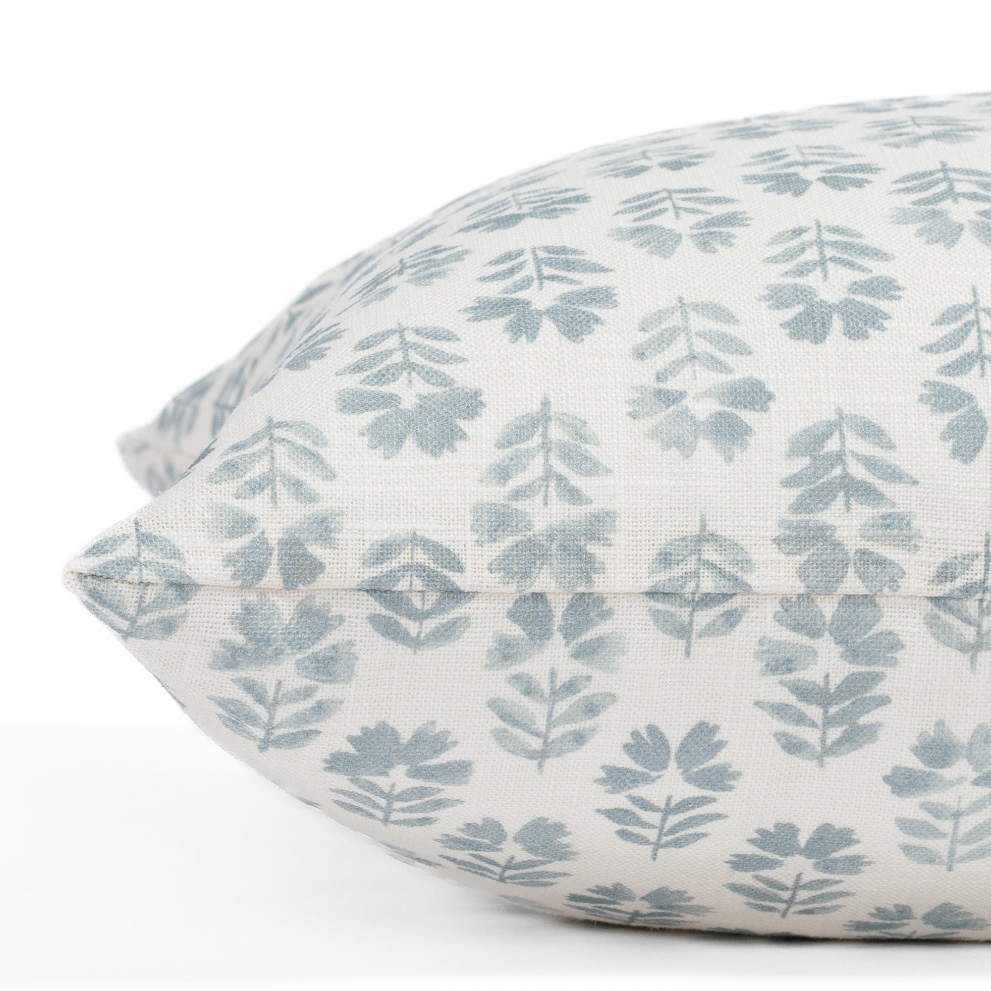 A blue and white floral block print pillow with a linen texture: close up side view.