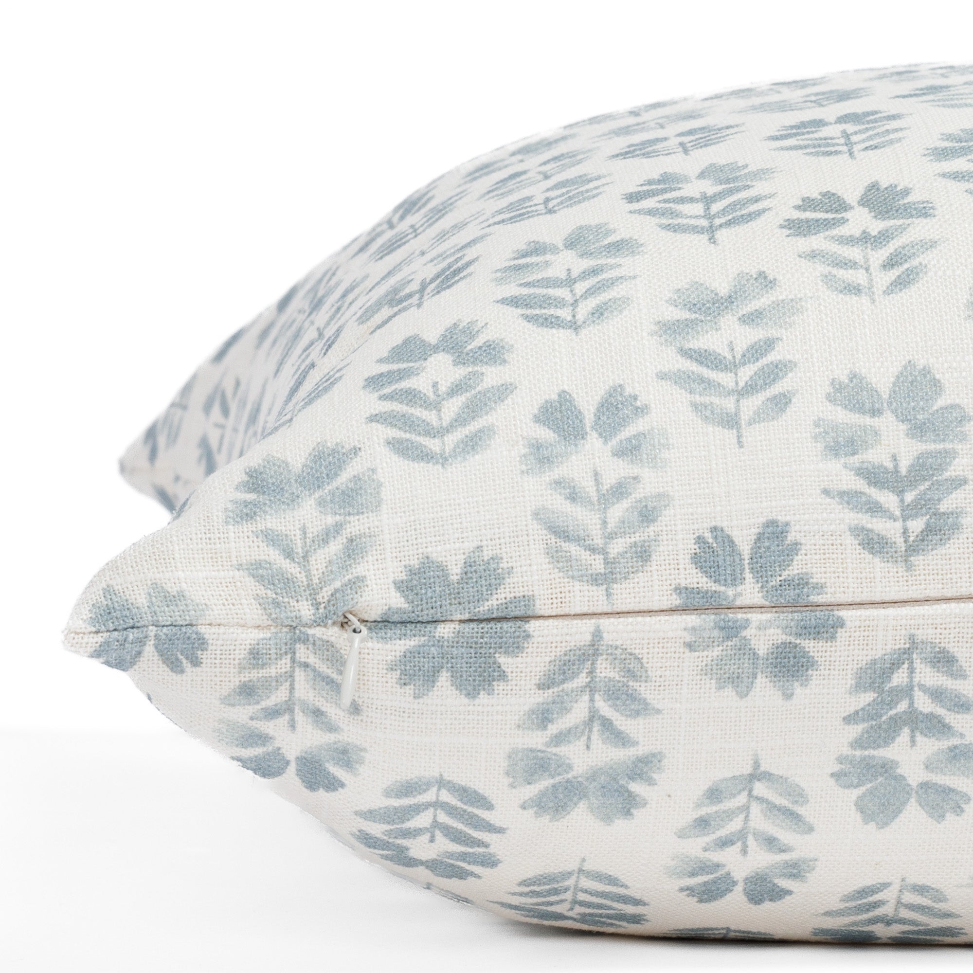 A cream designer throw pillow from Tonic Living with light blue flowers: a close up zipper view.