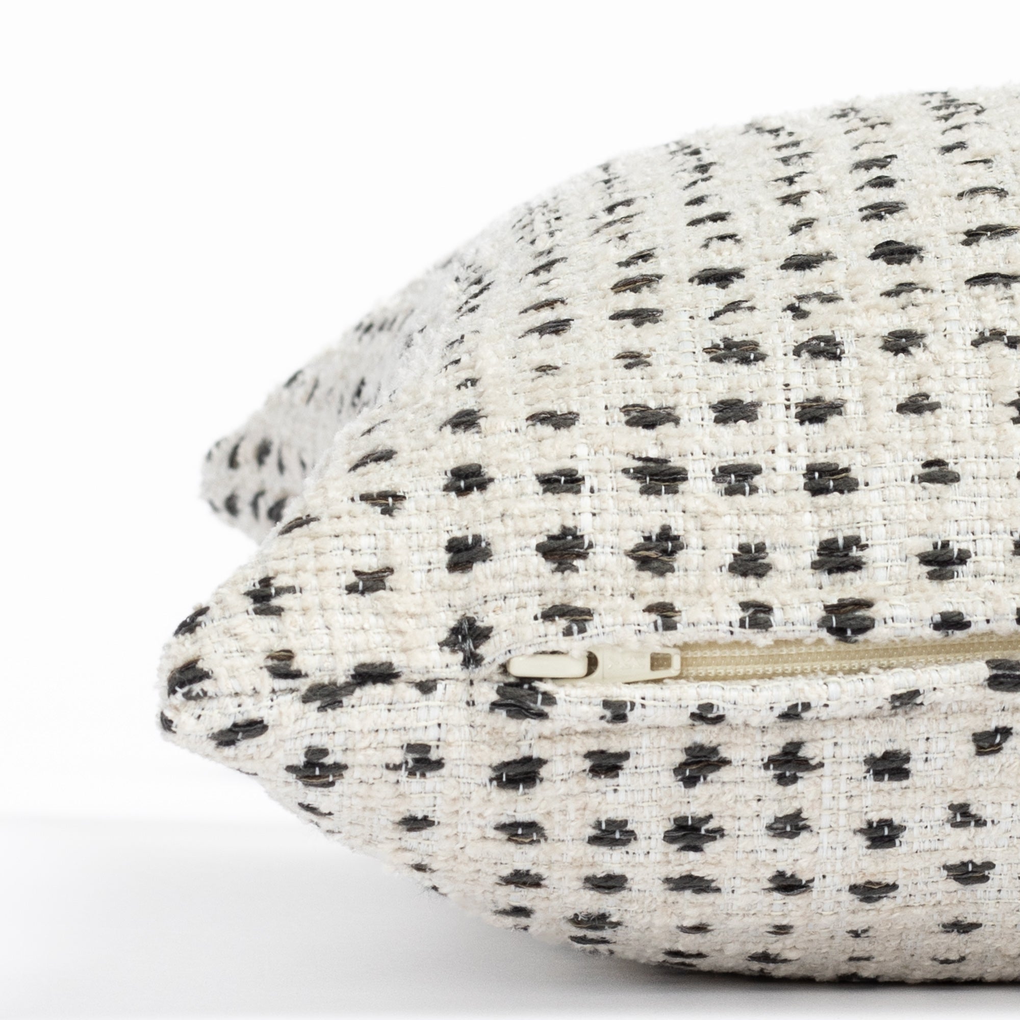 a cream and black polka dot patterned throw pillow : close up zipper view