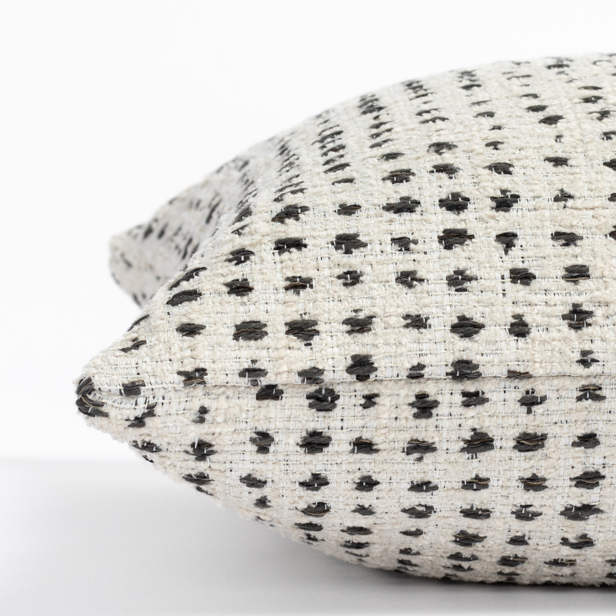 a cream and black polka dot patterned throw pillow : close up side view