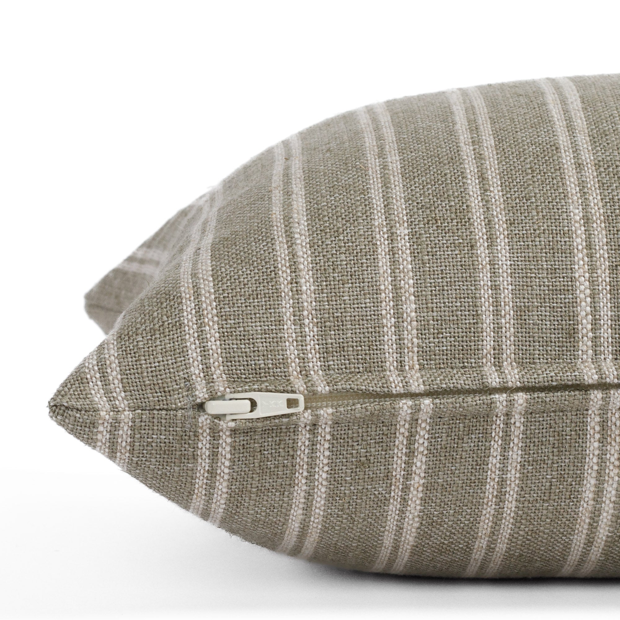 Side view of the Conway Stripe Sage 12x24 lumbar cushion by Tonic Living, showing the exposed zipper and slubby weave in dusty sage green and warm beige.