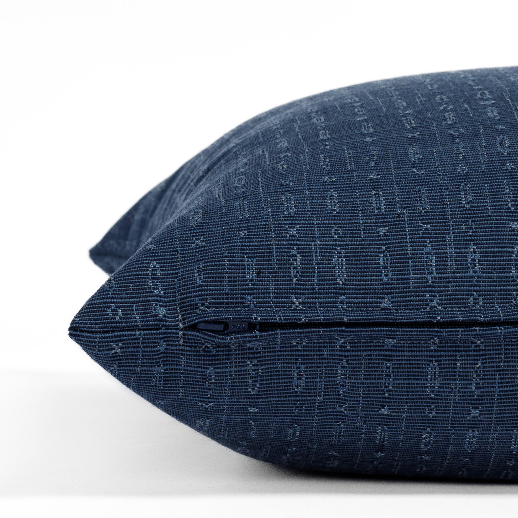 Embrace Indigo, a dark blue tone-on-tone textured pillow from Tonic Living, with a subtle abstract geometric design: close up zipper view.