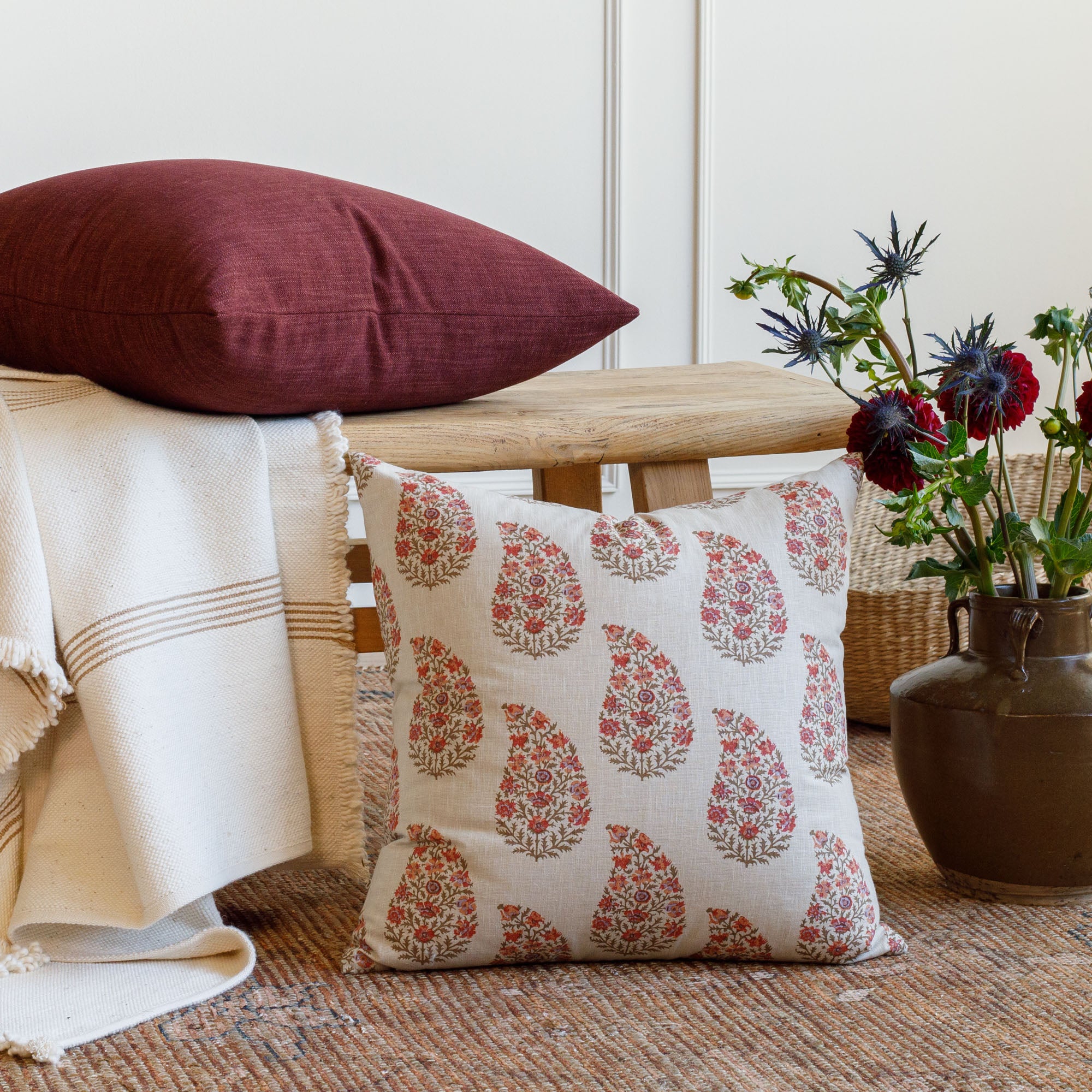 Grace 20x20 Throw Pillow, Rosewood and Bedford 22x22 Throw Pillow, Merlot by Tonic Living styled on a bench with flowers.