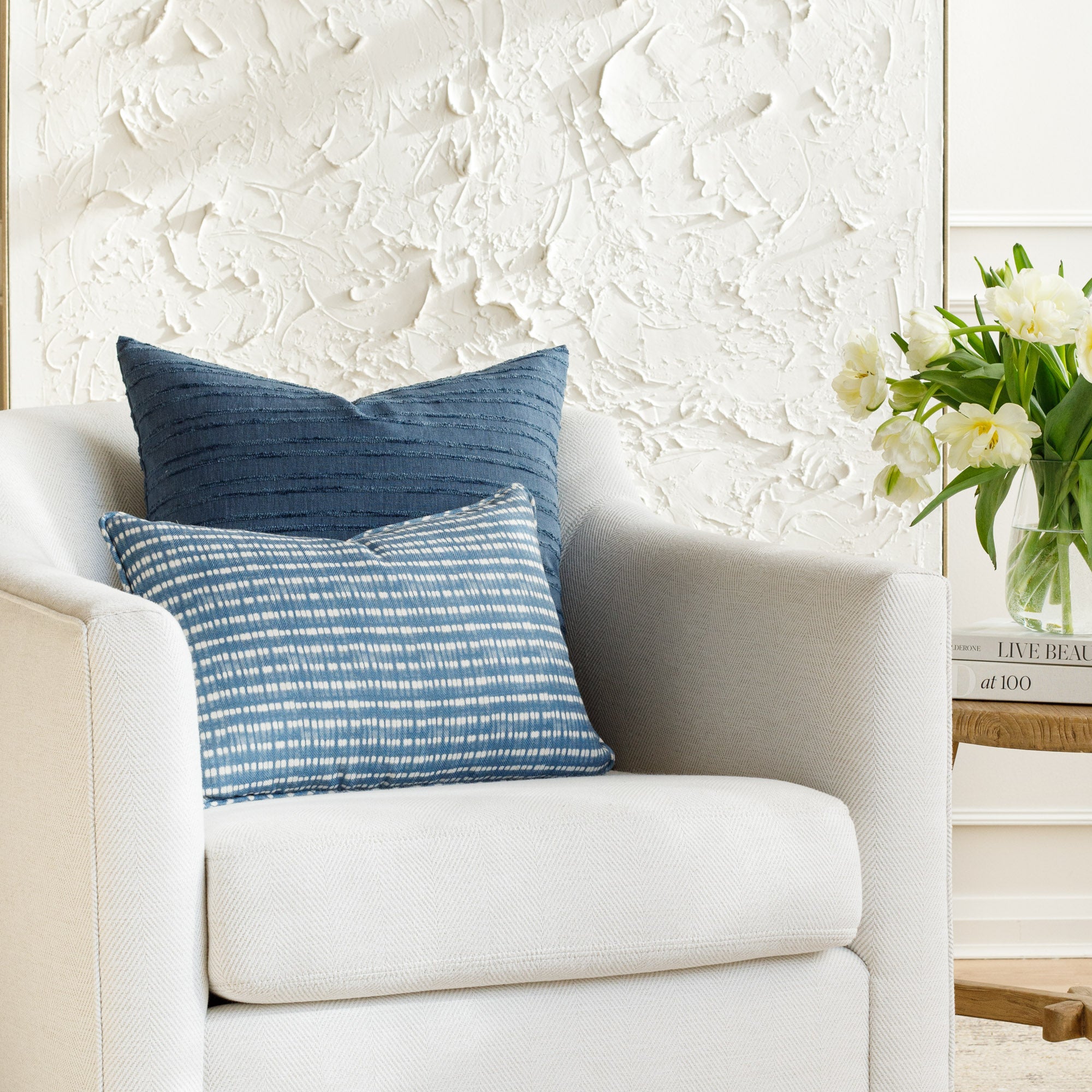 Two textured blue toss pillows styled on a white chair (Nile Indigo & Malibu Stripe Navy by Tonic Living).