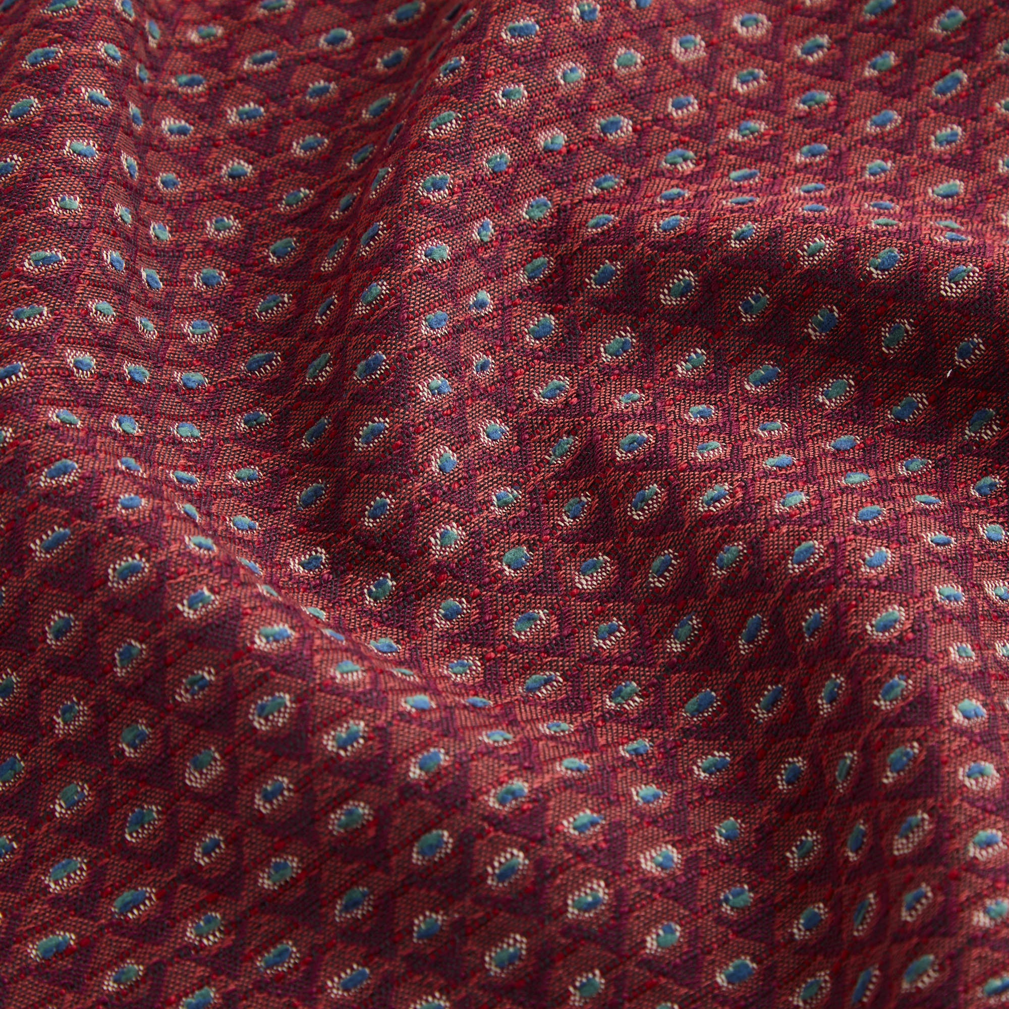 Close up of Pembrook Fabric Merlot, showcasing burgundy red woven diamond pattern with blue-green and natural accents from Tonic Living.