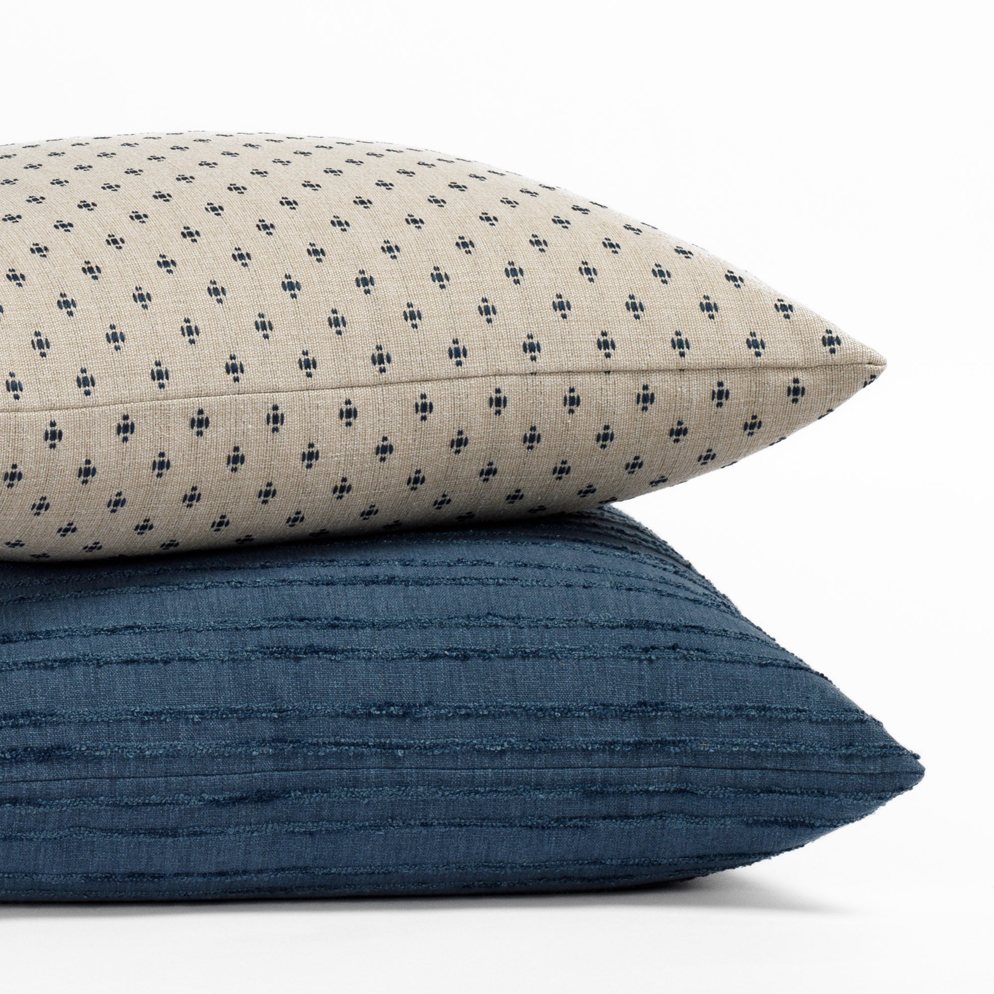A beige and navy patterned pillow resting on a navy textured stripe pillow.