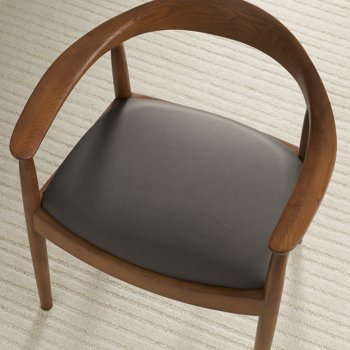 Tonic Living Smythe Charcoal faux leather upholstery fabric shown on a dining chair seat in a deep charcoal grey brown.
