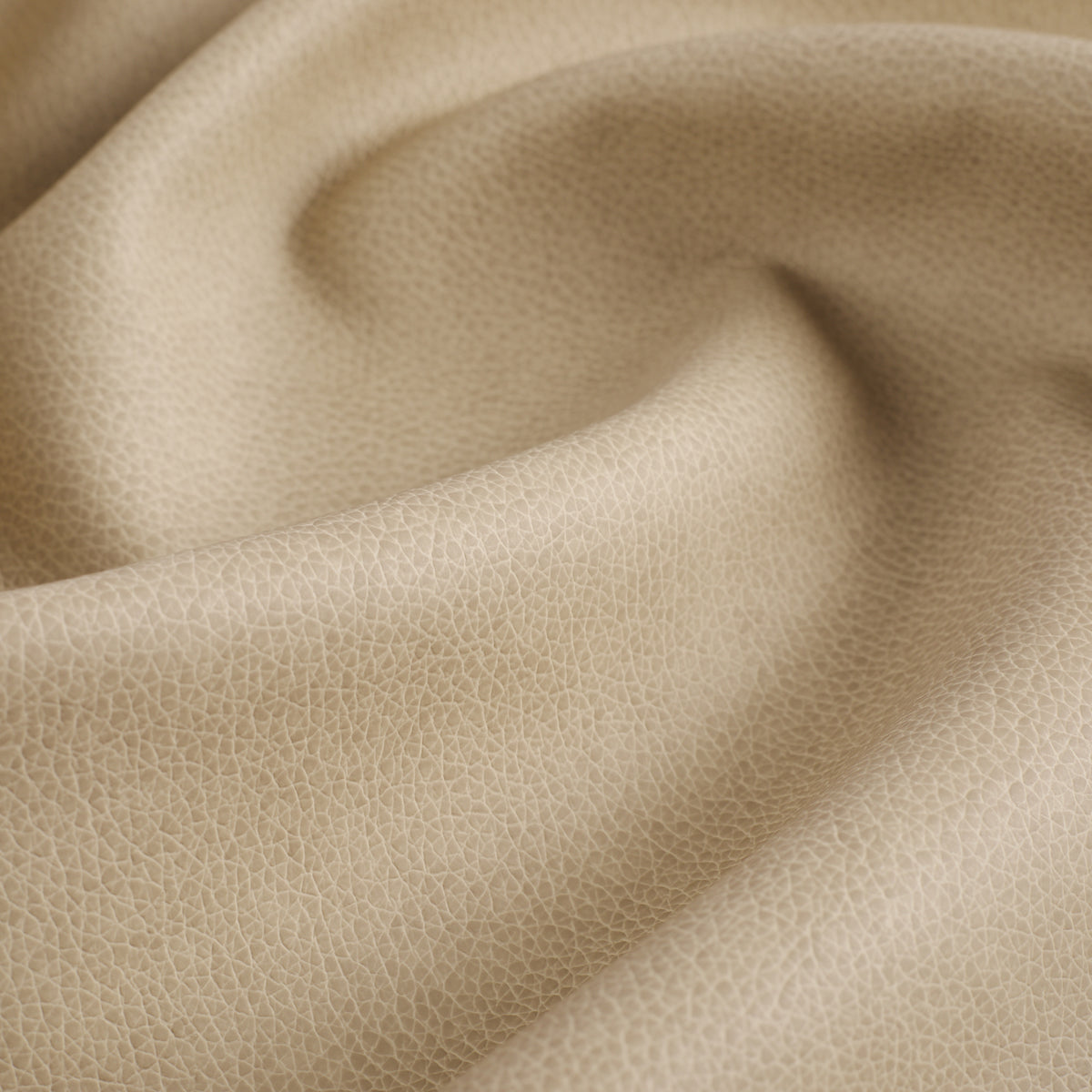 Close up of Tonic Living Smythe Sandstone faux leather upholstery fabric showing its sandy beige colour and realistic leather grain.