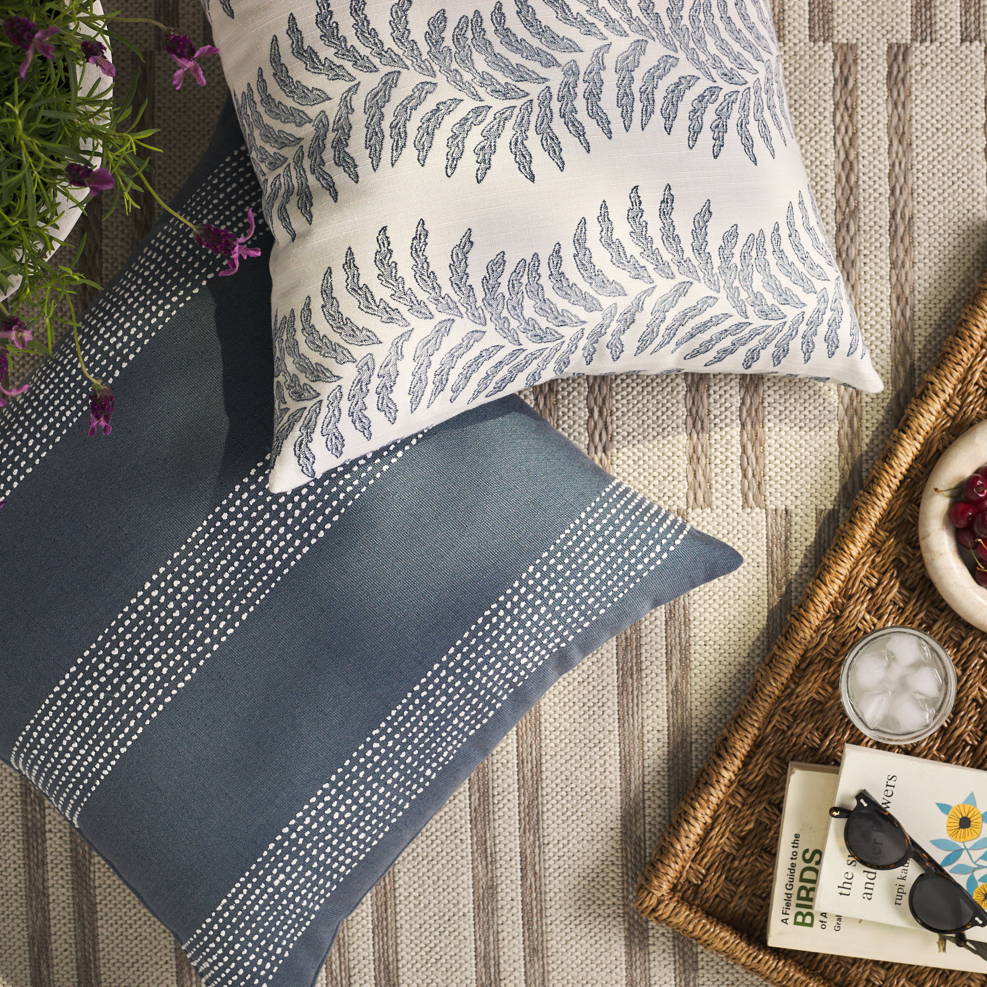 Overhead view of Tonic Living Swoon Denim blue decorative cushion with Caper Slate pillow on an outdoor rug.