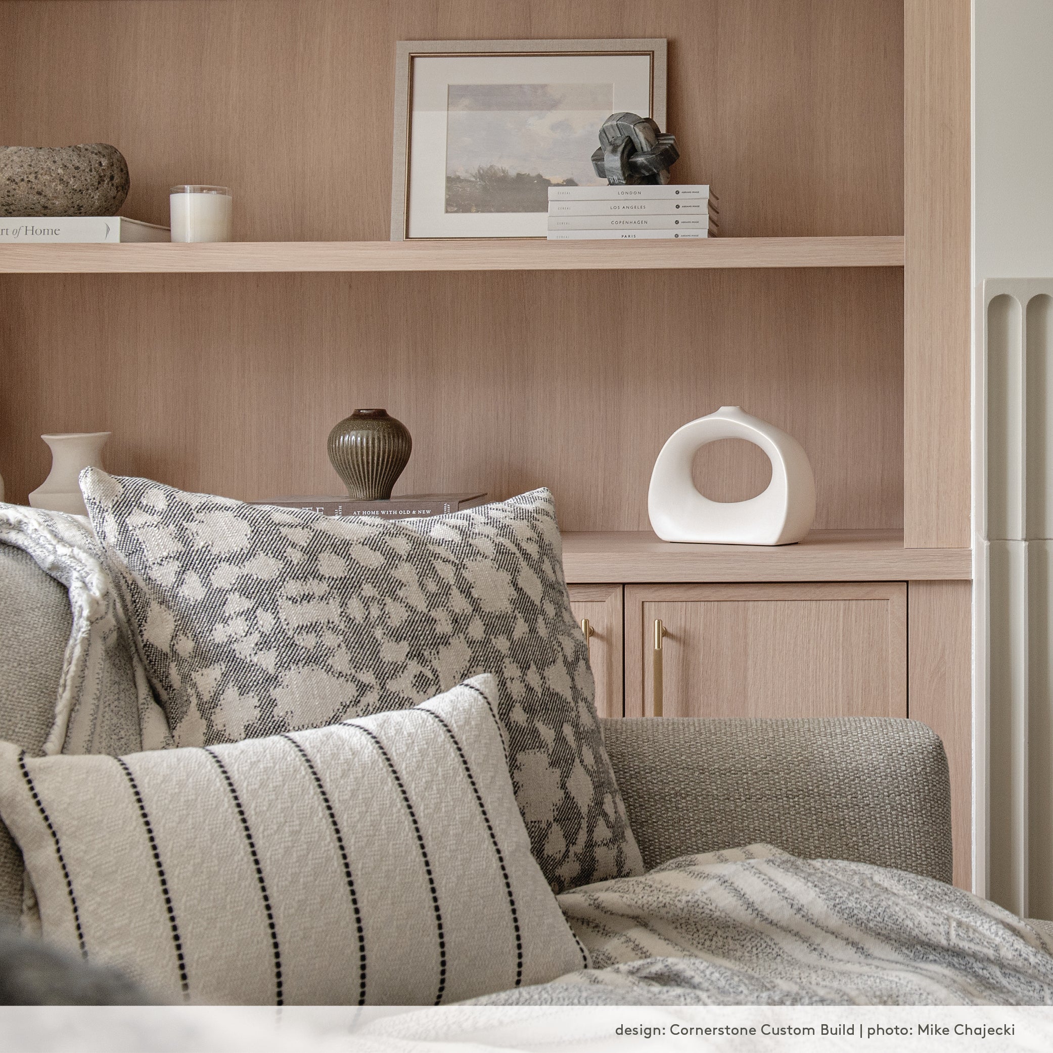 Black and white pillows on a light grey sofa in a modern organic living room with white oak built-in shelves.