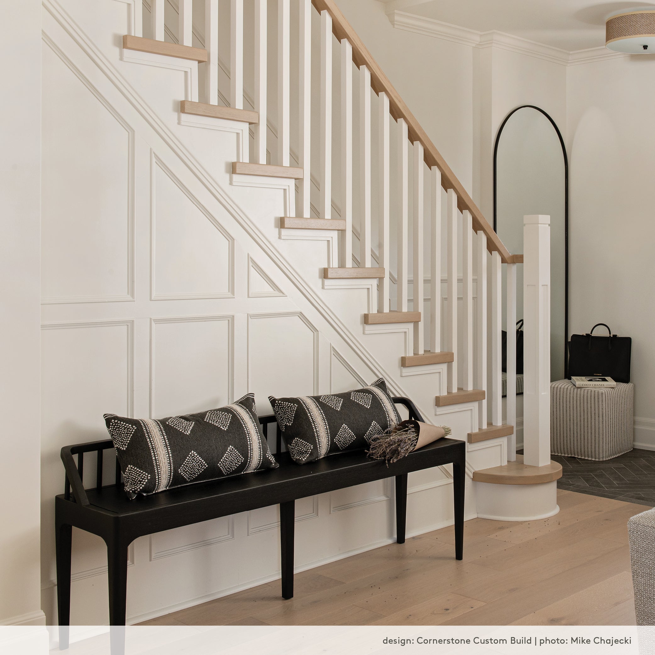 A contemporary black wood bench in a front hall with a white oak staircase and wall moulding.