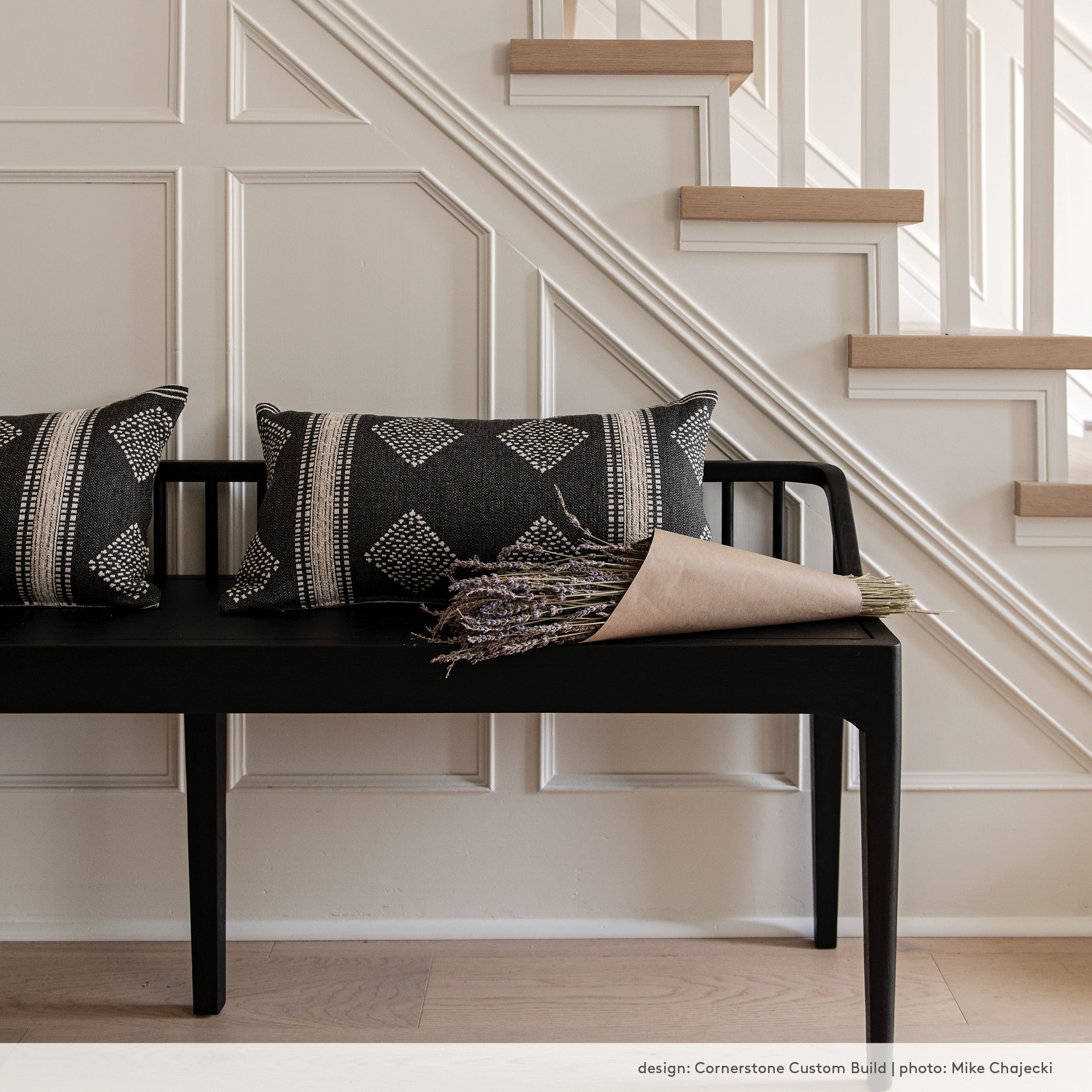 A contemporary black wood bench in a front hall with a white oak staircase and wall moulding.