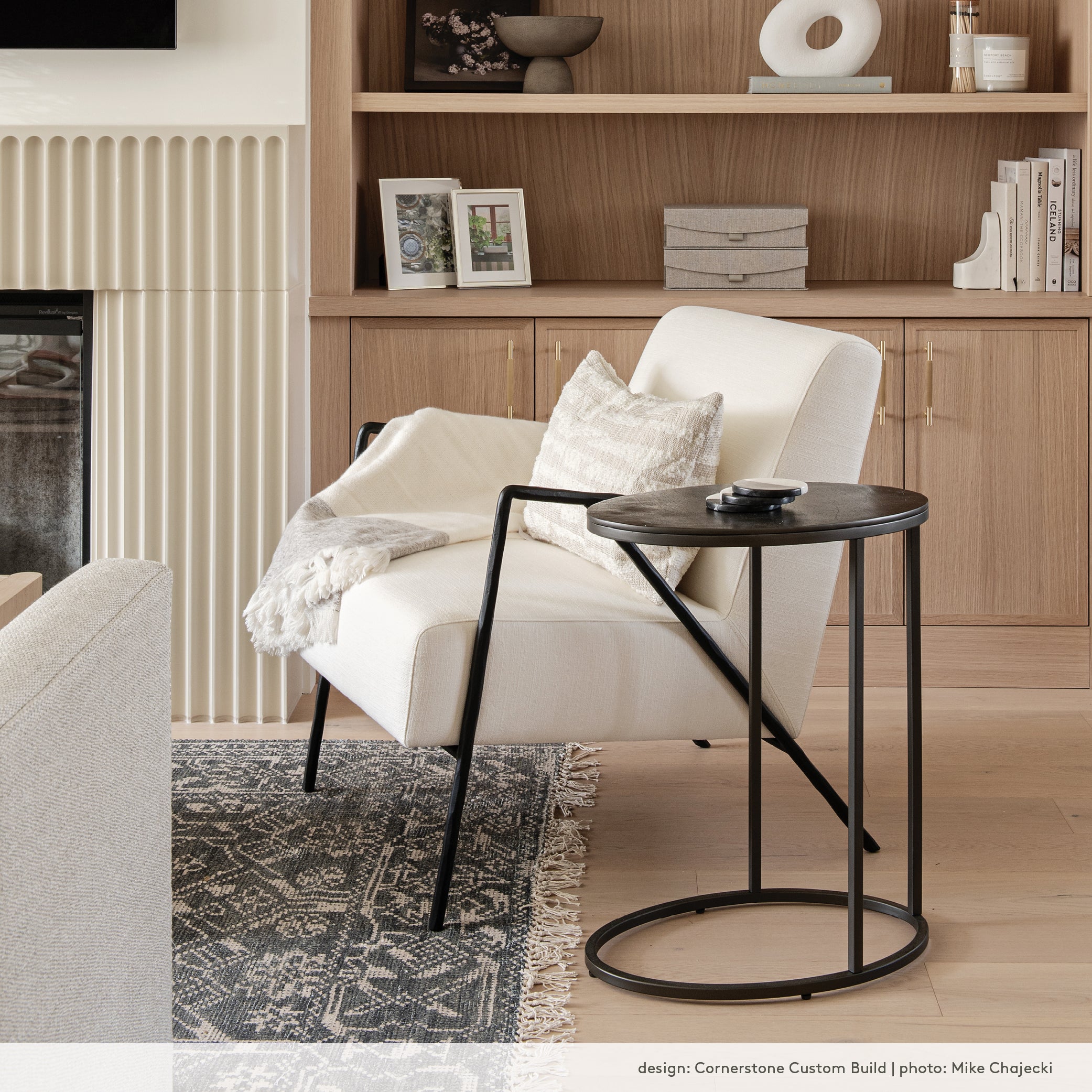 A contemporary black and white chair in an organic modern living room with white oak built in shelves and fluted detail around a fireplace.