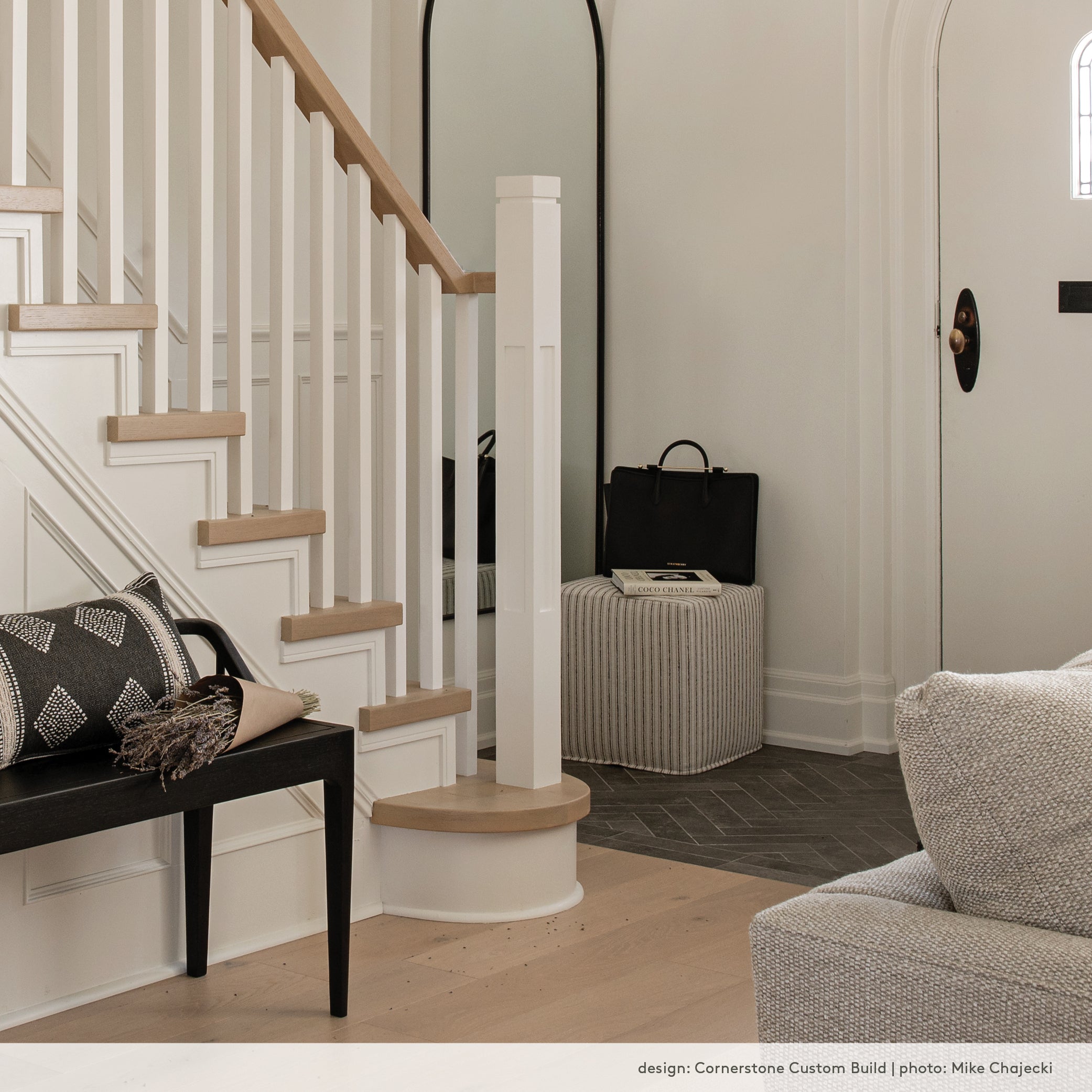 Front hall in a house with white oak floors and slake herringbone tile. Tonic living ottoman and black wood bench.