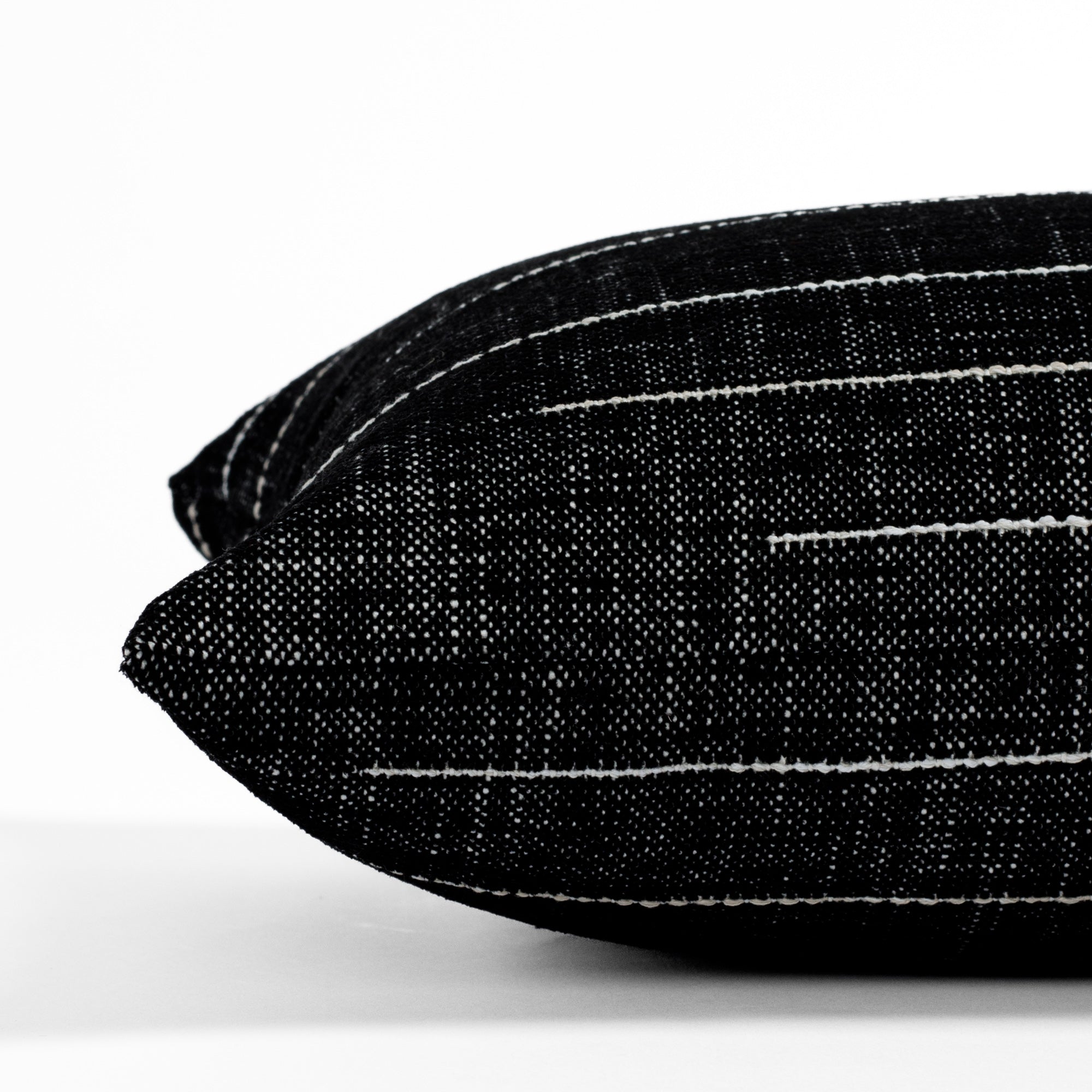 Yuzu Onyx, a black and white indoor/outdoor lumbar pillow from Tonic Living, showcasing a dappled texture accented with organic white stripes: close-up side view.
