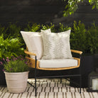 Tonic Living Swoon Sage decorative cushion styled on a chair with the Caper Linen 22x22 pillow outdoors.
