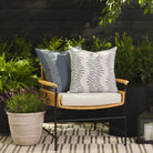 Tonic Living Swoon Denim outdoor cushion styled on a chair with Caper Slate 22x22 pillow in a outdoor patio setting.
