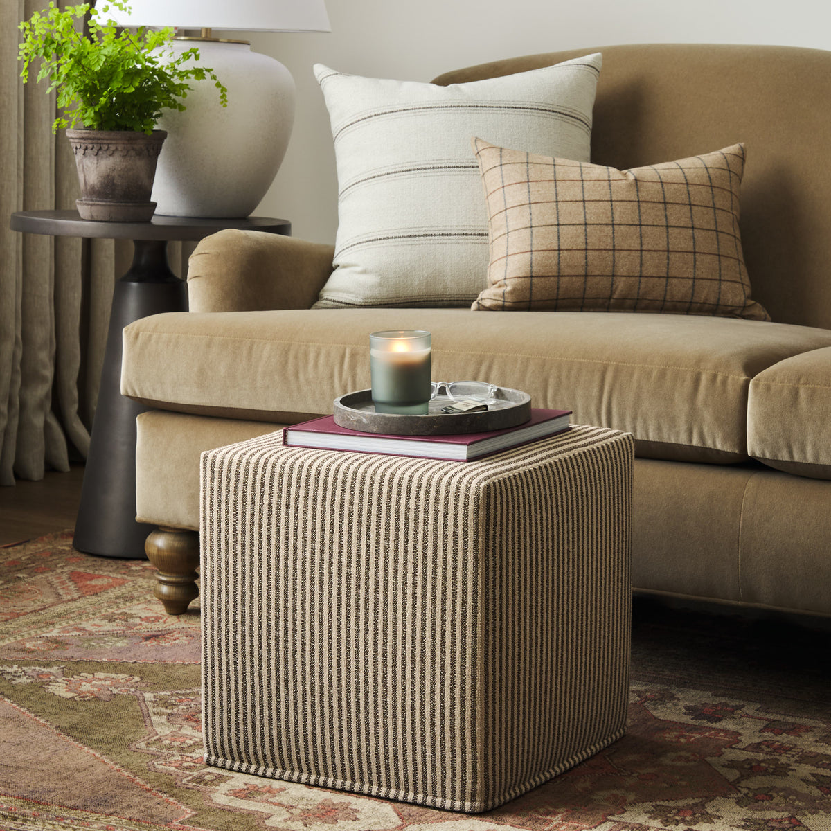 Tonic Living Crosby Stripe Truffle cube ottoman styled as an accent table in a warm neutral living room with striped and checked pillows.