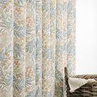 Tonic Living Fable Meadow botanical drapery fabric shown as curtains featuring leafy blue, terracotta, and brown motifs on a soft white ground.