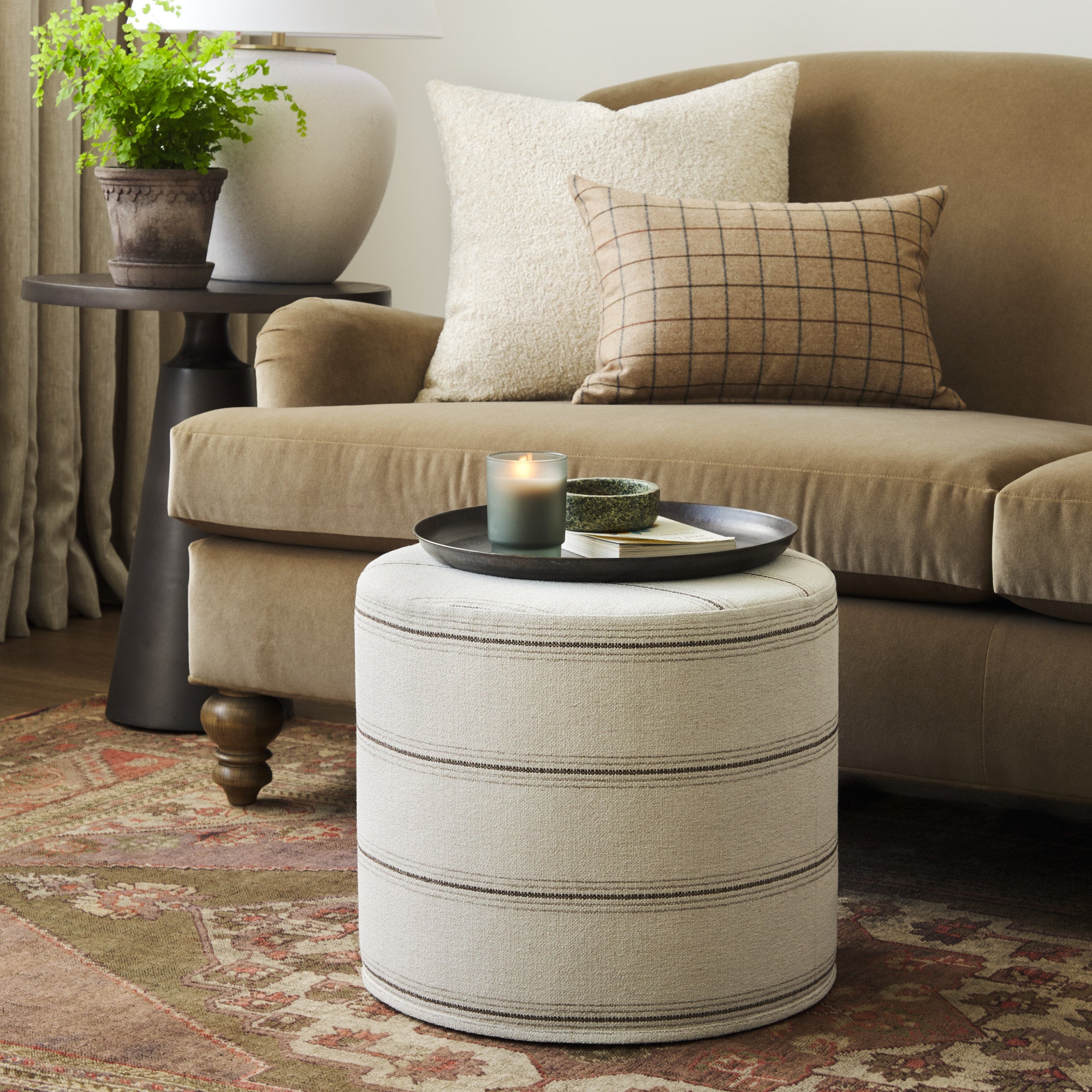 Tonic Living Gibson Stripe Birch round ottoman styled as an accent table in a warm neutral living room with coordinating throw pillows.