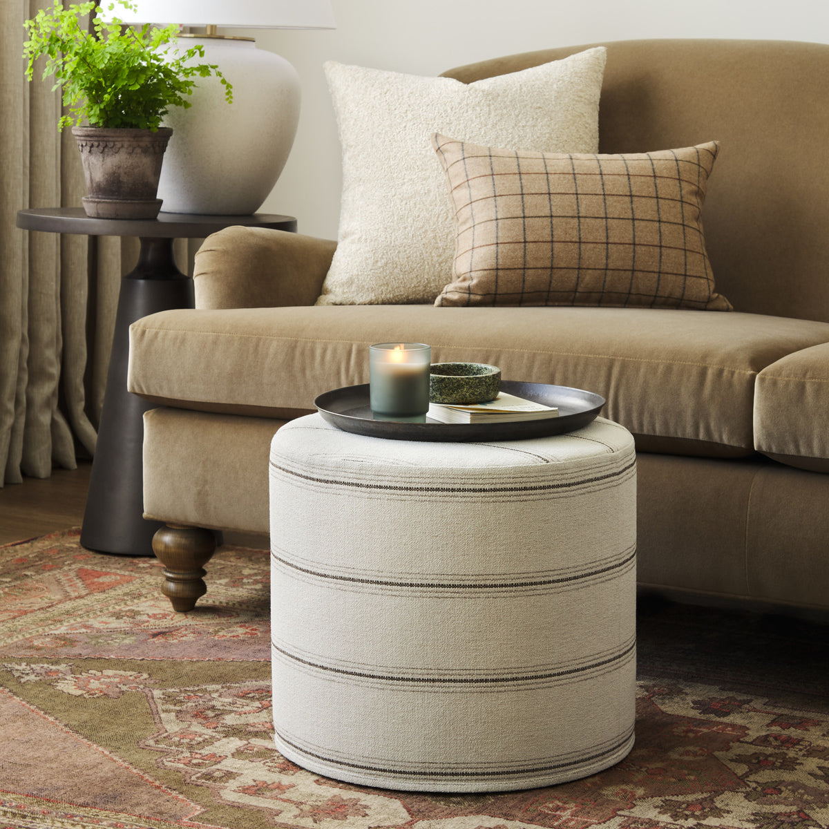 Tonic Living Gibson Stripe Birch round ottoman styled as an accent table in a warm neutral living room with coordinating throw pillows.