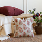 Grace 20x20 Throw Pillow, Rosewood and Bedford 22x22 Throw Pillow, Merlot by Tonic Living styled on a bench with flowers.