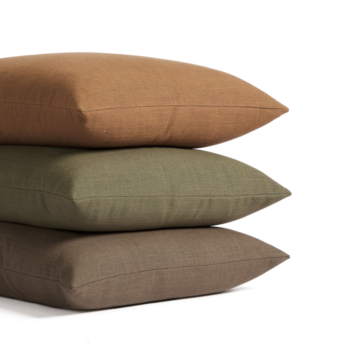 Stack of Tonic Living Hampton pillows in Cinnamon russet brown, Moss earthy green, and Walnut dark brown with linen-inspired texture.