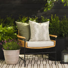 Tonic Living Swoon Sage outdoor cushion styled on a chair with Hawthorne Basil 22x22 pillow in a green outdoor setting.