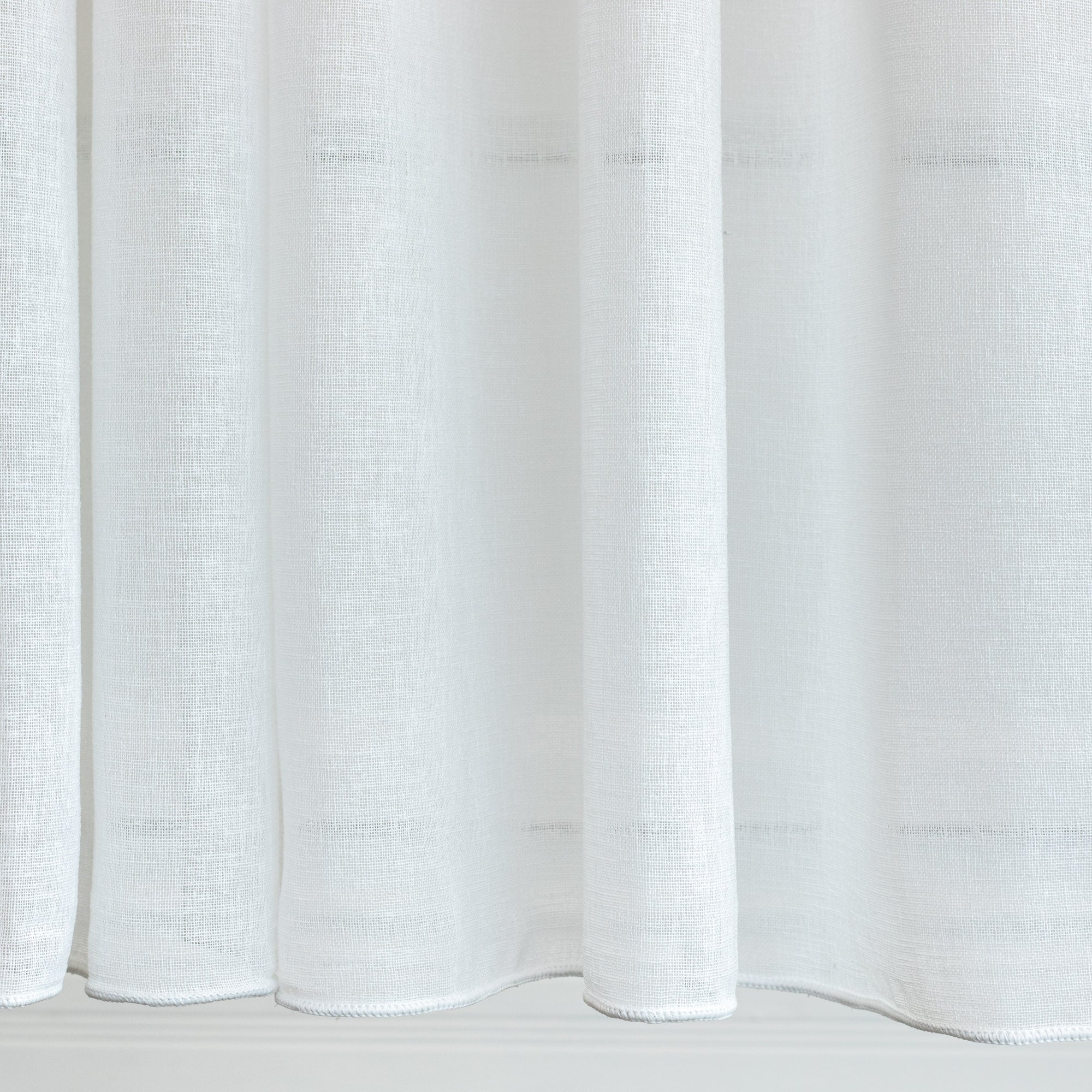 a soft white sheer drapery fabric : close up view of weighted edge