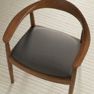 Tonic Living Smythe Charcoal faux leather upholstery fabric shown on a dining chair seat in a deep charcoal grey brown.