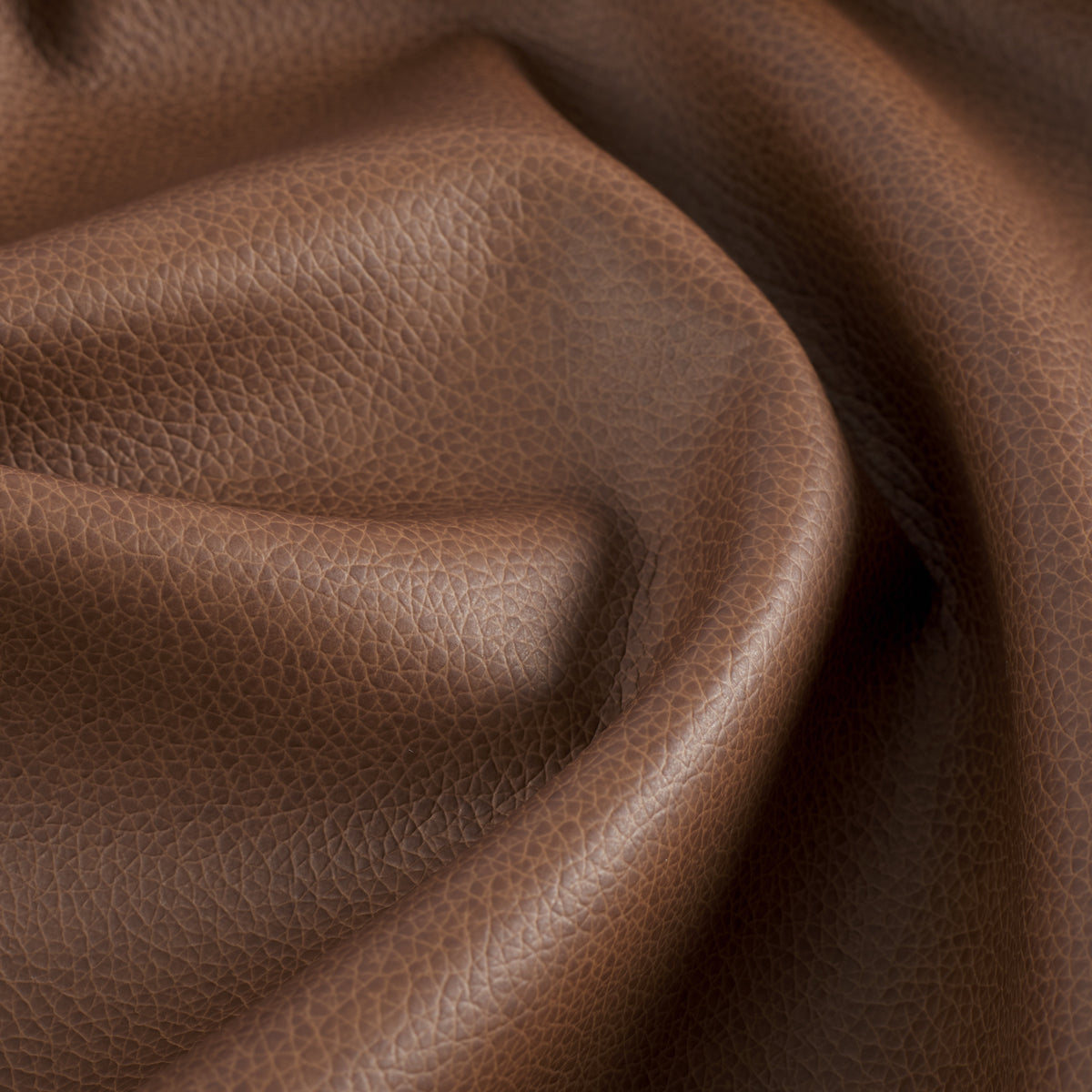 Close up of Tonic Living Smythe Cognac faux leather upholstery fabric showing its deep cognac brown colour and realistic leather grain.