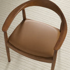 Tonic Living Smythe Saddle faux leather upholstery fabric shown on a dining chair seat in a warm saddle brown.