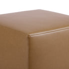 Close up of Tonic Living Smythe Saddle cube ottoman showing its saddle brown faux leather upholstery, natural-looking grain, and tailored corner detail.