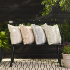 Tonic Living Swoon pillow collection in sand, terracotta, denim blue, and sage green styled on an outdoor bench.