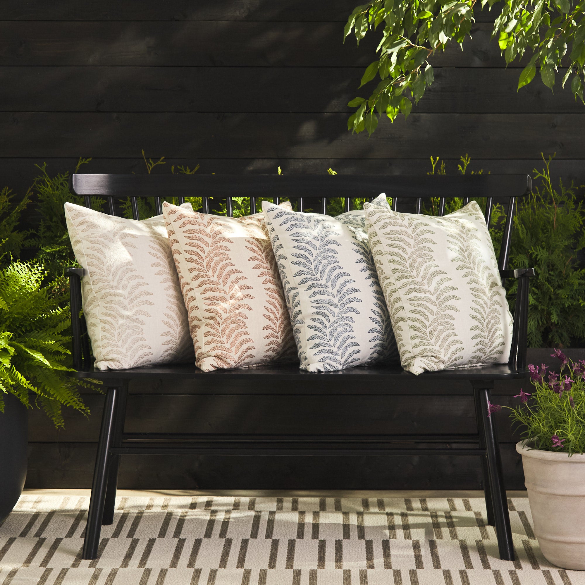 Tonic Living Swoon pillow collection in sand, terracotta, denim blue, and sage green styled on an outdoor bench.