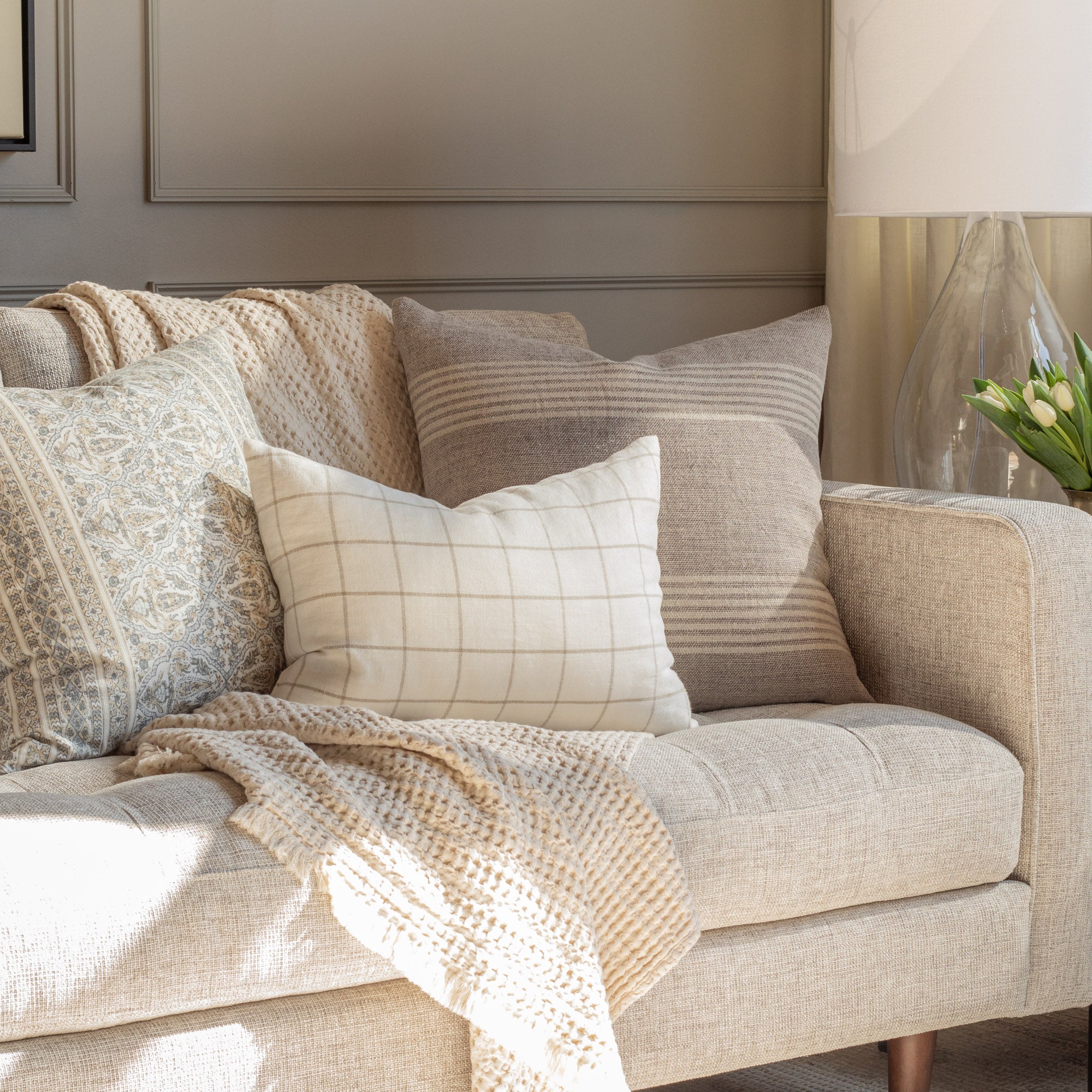 Throw pillows on a sofa with natural tones and earthy textures - living room scene by Tonic Living