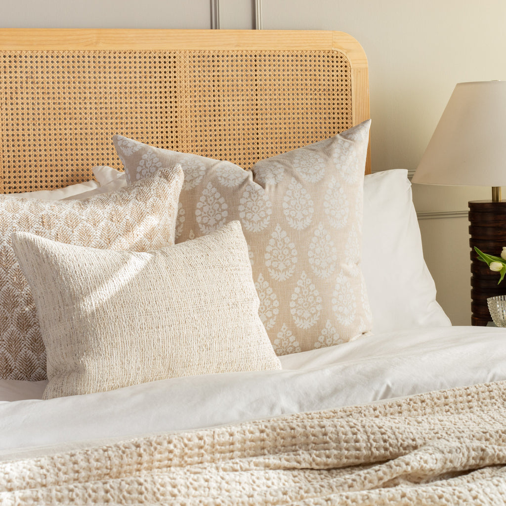 A linen-toned throw pillow with a simple and elegant pattern of white block print medallions in a neutral trip setting on a queen bed