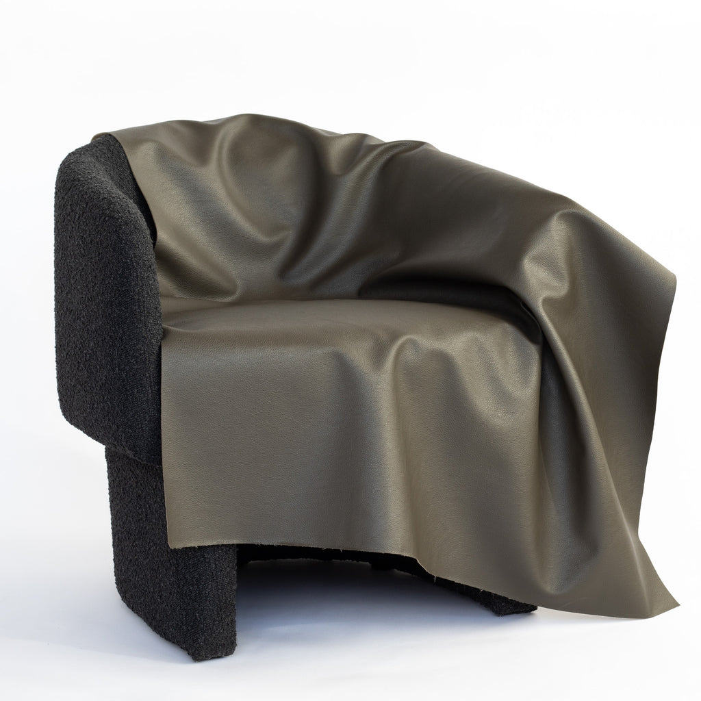 a charcoal gray with a subtle moss undertone performance vinyl faux leather upholstery fabric draped on a chair