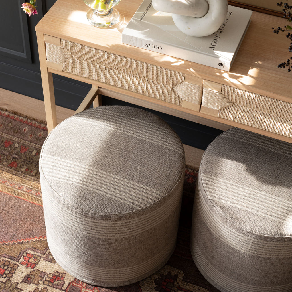 a natural tan and faded black striped linen round ottoman : tucked under a console